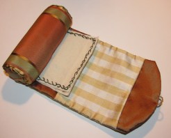 This case is made with a lovely fall toned striped silk on the exterior and a coppery shot silk on the interior. The spacious pocket is a white and golden yellow plaid silk. The two off white wool needle-pages are vine stitched with dark green on the first and golden yellow on the second. The viney stitch is continued on the ends of the cotton batted roll. The case is held closed with a tiny mother of pearl button and loop. This case is entirely hand-sewn and based on an original formerly in my collection and featured in the up-coming  Fanciful Utility. This case took approx. 5 hours to hand-sew.