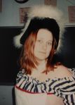 Anna ca 1998-99 dressed in a black and white striped shift, red pinstripe wool pair of stays, white, apron, and black wool felt hat with white feathers. 